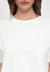 White cotton t-shirt with an embossed "MICHAEL KORS" logo in matching thread. Features a round neckline and short sleeves.