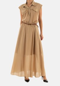 Vestido maxi sin mangas beige con botones en la parte delantera, dos bolsillos en el pecho, cintura ceñida y falda transparente. Combinado con tacones negros.