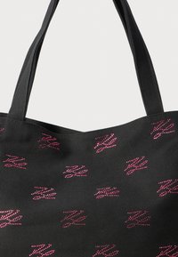 Black fabric tote bag with two handles and scattered small pink rhinestone designs shaped like stylized hands or claws.