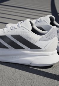 White running shoes with gray accents, structured mesh upper, three dark stripes, and "DURAMO SL2" branding. LightMotion sole technology.