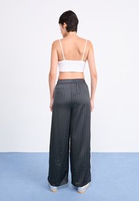 Wide-leg, pinstriped pants in dark gray, featuring an elastic waistband. Paired with a white cropped top and silver sneakers.
