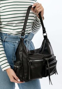 Sac épaule en cuir noir avec plusieurs poches zippées, une texture lisse et une bandoulière réglable. Le design comprend des franges pendantes.