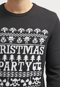 Pull en tricot noir avec des motifs festifs blancs, comprenant des arbres, des crânes et le texte "CHRISTMAS PARTY". Encolure ronde, tissu texturé.