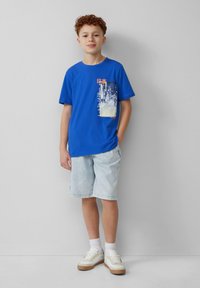Blauwe katoenen t-shirt met een grafisch zakontwerp met Japanse tekst, gecombineerd met lichte denim shorts en witte sneakers.