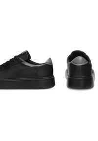 Čierne kožené tenisky majú hladký povrch, zaoblenú špičku a kontrastný sivý akcent na päte. Hrubá podrážka s minimalistickými dizajnovými prvkami.