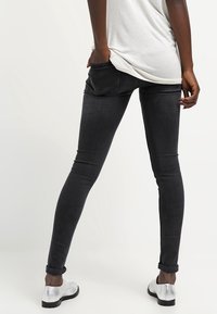 Black skinny jeans with a smooth texture, featuring a mid-rise waist and rolled cuffs. Worn with silver flat shoes.