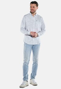 Gestreiftes Hemd aus hellblauem und weißem Baumwollstoff, mit Knopfleiste, reguläre Passform, kombiniert mit hellblauen Jeans aus Denim und beigen Sneakers.