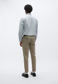 Ριγέ πουκάμισο με κουμπιά σε ανοιχτό μπλε και λευκό, μπεζ παντελόνι και μαύρα παπούτσια. Ορατή ραφή στο πουκάμισο, δύο πίσω τσέπες στο παντελόνι.