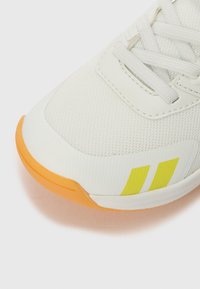 Adidași sport din plasă albă cu talpă de cauciuc portocalie, cu dungi galbene și accente texturate în partea superioară și pe șireturi.