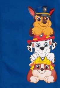 T-shirt blu con tre cani dei cartoni animati impilati verticalmente. Il cane in cima è marrone con un cappello blu, quello al centro è bianco con macchie nere e quello in fondo è marrone chiaro con un cappello giallo.