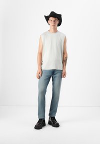 Mouwloos lichtgrijs topje, vervaagde blauwe jeans en een zwarte cowboyhoed. Zwarte chunky laarzen maken de outfit compleet. Eenvoudig, casual ontwerp.