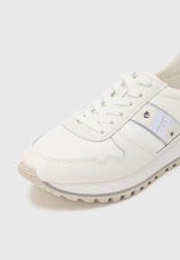 Baskets blanches avec tige synthétique lisse, fermeture à lacets, accents argentés et semelle en caoutchouc texturée. Dotées d'un design cousu et d'une étiquette logo.