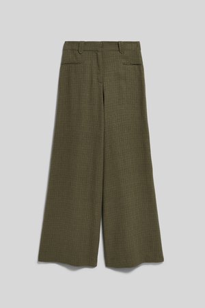 Kvinde med krøllet hår iført oversized olivengrøn ternet jakkesæt med vidde benbukser og bælteblazer, stående mod en ensfarvet baggrund.