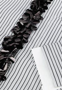 Zwart-wit gestreepte stof met een gestructureerde zwarte versiering met ovale vormen langs het midden, en een opgevouwen witte manchet aan de onderkant.