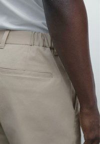 Beige trousers with an elastic waistband, featuring a back pocket, smooth texture, and straight leg design. Neutral color enhances versatility.
