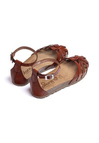 Sandali in pelle marrone con design a strappi, fibbia regolabile alla caviglia e soletta testurizzata. Suola flessibile e soletta in sughero per il comfort.