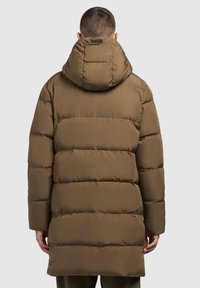 Pruun puffertaken, millel on horisontaalsete õmblustega sektsioonid, suur kapuuts ja varjatud esi-taskud, loodud soojuse ja mugavuse jaoks.