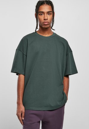 Mørkegrøn oversized t-shirt lavet af bomuld. Den har en rund halsudskæring og korte ærmer, med en glat tekstur og minimale sømme.