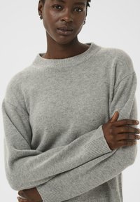 Pullover grigio chiaro realizzato in un morbido tessuto testurizzato. Presenta un colletto a girocollo e polsini a costine con una vestibilità oversize.