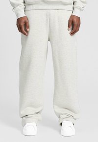 Hellgraue Sweatpants mit entspannter Passform, weichem Material, elastischem Bund und subtiler Textur. Kombiniert mit weißen Sneakern.