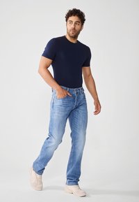 Marineblå kortermet t-skjorte med tettsittende passform, kombinert med lyseblå bukser med rette ben og beige joggesko, med klassisk lomme-design.