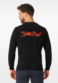 Felpa nera con una grafica audace e multicolore "Spring Break" sulla schiena. Polsi e orlo a costine. Tessuto morbido e texturizzato.