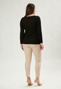 Schwarzer Strickpullover mit einem strukturierten Zickzackmuster, kombiniert mit beigen, figurbetonten Hosen und goldenen, geschnürten High Heels.