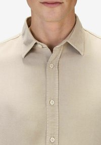 Vaalean beige-painettu kauluspaita, joka on valmistettu sileästä kankaasta. Paidassa on tavallinen kaulus, kuusi nappia edessä ja hienostunut kiilto.