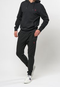 Black hoodie and joggers made of cotton blend, featuring a front pocket and small red logo. Smooth texture, relaxed fit, with elastic cuffs.