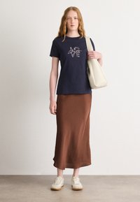 Navy t-shirt with graphic "LOVE" in metallic accent, paired with a brown satin midi skirt. Model carries a beige shoulder bag. White sneakers.