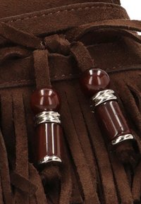 Material de ante marrón con detalles de flecos largos. Dos componentes decorativos: una cuenta de color rojo oscuro y una pieza cilíndrica, cada uno con acentos plateados.