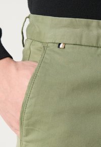 Pantaloni in misto cotone verdi con una vestibilità rilassata, tasche laterali e un piccolo dettaglio a bandiera multicolore in vita.