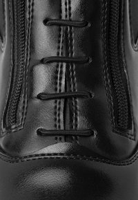 Zapato de cuero negro con costuras elevadas, superficie texturizada, cordones y un detalle de cremallera expuesto a lo largo del costado.