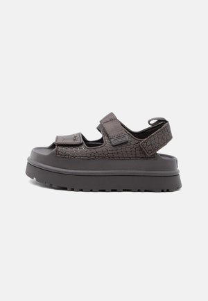 Sandale cu talpă groasă și curele texturate de culoare maro închis, cu două închideri Velcro reglabile pe deasupra piciorului și una în jurul călcâiului, design cu vârf și călcâi decupați.