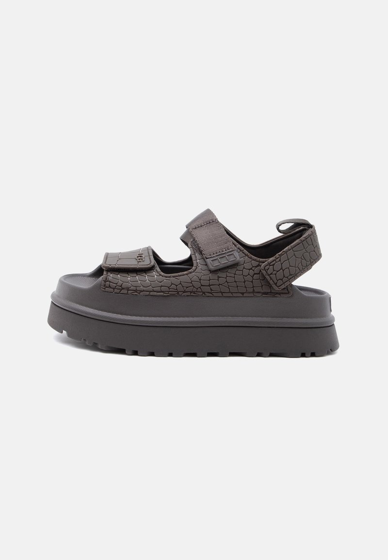 Πέδιλο με χοντρή σόλα και σκούρες καφέ υφασμάτινες λουρίδες, δύο ρυθμιζόμενα κλείσιμο με βέλκρο πάνω από το πόδι και ένα γύρω από τη φτέρνα, ανοιχτό σχέδιο στα δάχτυλα και τη φτέρνα.