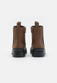 Bottines en cuir marron avec des panneaux élastiques noirs sur les côtés, des languettes de tirage et des semelles épaisses en caoutchouc noir. Texture lisse et détails piqués.