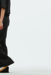 Crne, prostrane hlače širokih nogavica, izrađene od laganog materijala. Dizajn ima minimalne akcentne detalje i čistu siluetu.