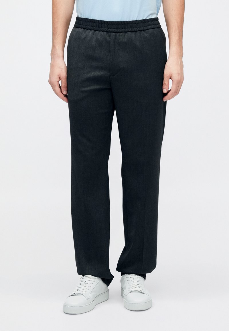 Dunkelgraue, locker sitzende Hose mit elastischem Bund, die eine glatte Textur und zulaufende Beine aufweist, kombiniert mit weißen Sneakers.