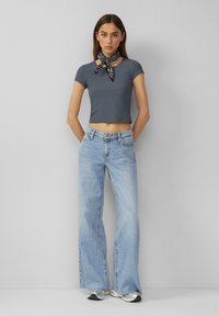 Šedý žebrovaný crop top v kombinaci se světle modrými zvonovými džíny. Modelka doplnila outfit černobíle vzorovaným šátkem kolem krku.