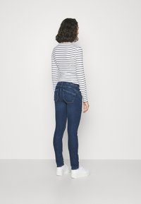 Jeans de mezclilla azul ajustados con dos bolsillos traseros, combinados con una camiseta de manga larga a rayas ajustada y zapatillas de plataforma blancas.