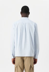 Light blue checkered long-sleeve shirt with a button-down collar, back pleat detail, and button cuffs, paired with khaki cargo pants.