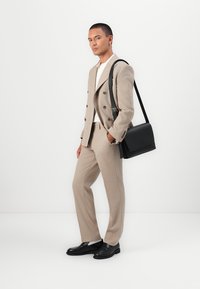 Beige double-breasted suit with matching trousers, white shirt underneath, black leather shoes, and a black messenger bag. Smooth textures.
