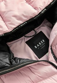 Gaišā rozā krāsā ar melniem akcentiem, ar mīkstu apdari iekšpusē. Aprīkots ar rāvējslēdzēju un etiķeti ar tekstu "BAKER by Ted Baker London." Gluda tekstūra.
