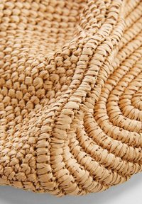 Alfombra de fibra natural tejida, hecha de un material texturizado de color beige claro, con un patrón circular y un borde ligeramente elevado para mayor detalle.