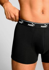 Black boxer shorts with a fitted design, made of stretchy fabric. Features a wide elastic waistband with white "PUMA" branding.