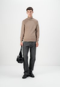 Bruine geribde coltrui, grijze jeans, zwarte tas en zwarte schoenen. Gladde textuur, aansluitend ontwerp en ronde halslijn.