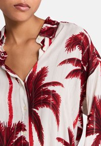 Camicia button-up rossa e bianca con stampa di palme, realizzata in un tessuto testurizzato e caratterizzata da un motivo a righe sottile, con dettagli visibili sul colletto.
