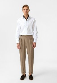 Witte button-up shirt, met een gestreepte bruine binnenkraag, geplooide beige broek, opgezette mouwen en zwarte instappers. Eenvoudig en op maat gemaakt ontwerp.