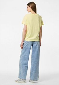 T-shirt di cotone gialla con scollatura rotonda, maniche corte e vestibilità rilassata, abbinata a jeans in denim azzurro chiaro a gamba larga.