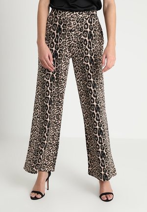 Kvinde iført højtaljede bukser med vide ben og leopardmønster, kombineret med sorte højhælede sandaler med åben tå.